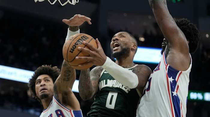 Bucks guard Damian Lillard shoots between 76ers players Kelly Oubre Jr. and Joel Embiid during the second half of a game.